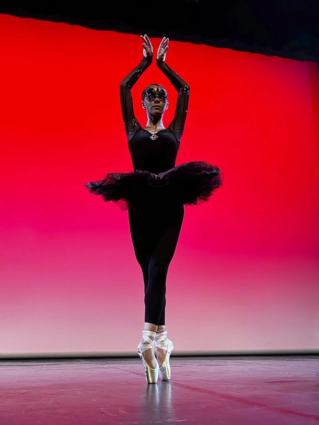 Danseuse classique en noir sur pointes devant un fond de scène rouge